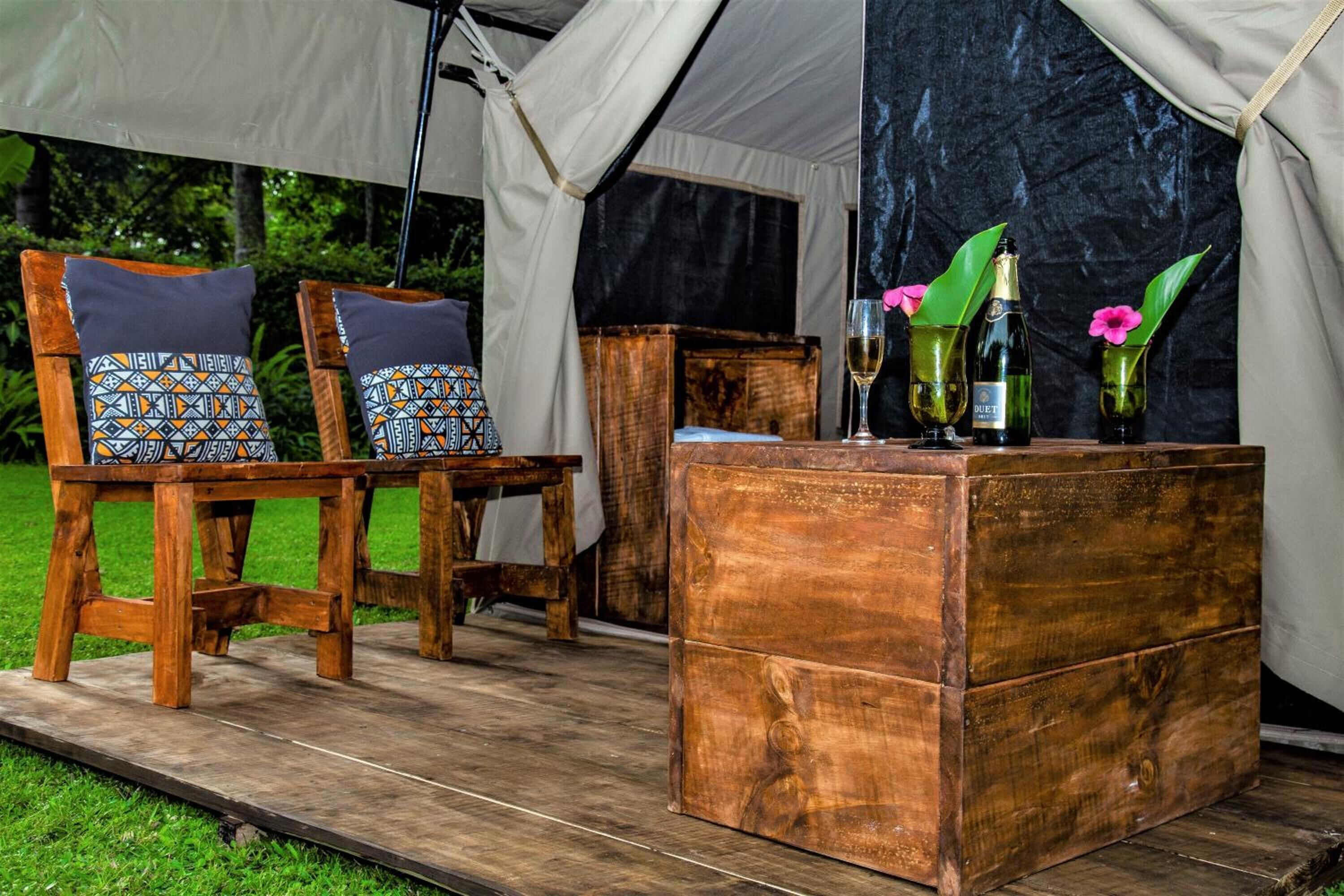A tent with two wooden chairs, a wooden chest, and a table with drinks and flowers.