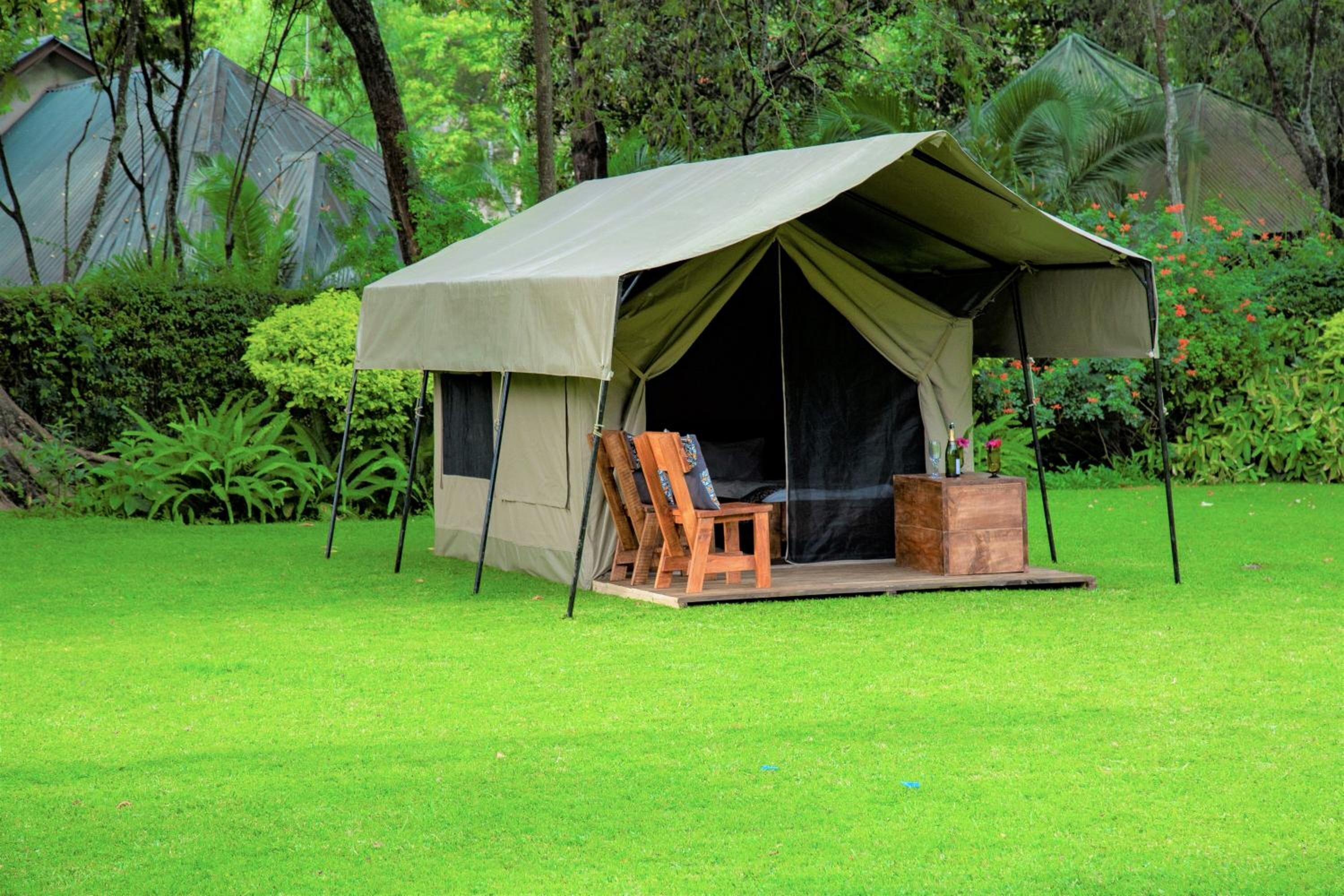 A tent with a wooden chair and a table in a grassy area surrounded by trees.