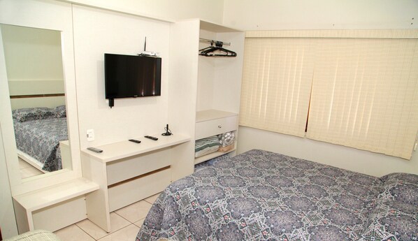 Une chambre à coucher comprenant un lit, un téléviseur fixé au mur, une armoire et une fenêtre avec des stores.