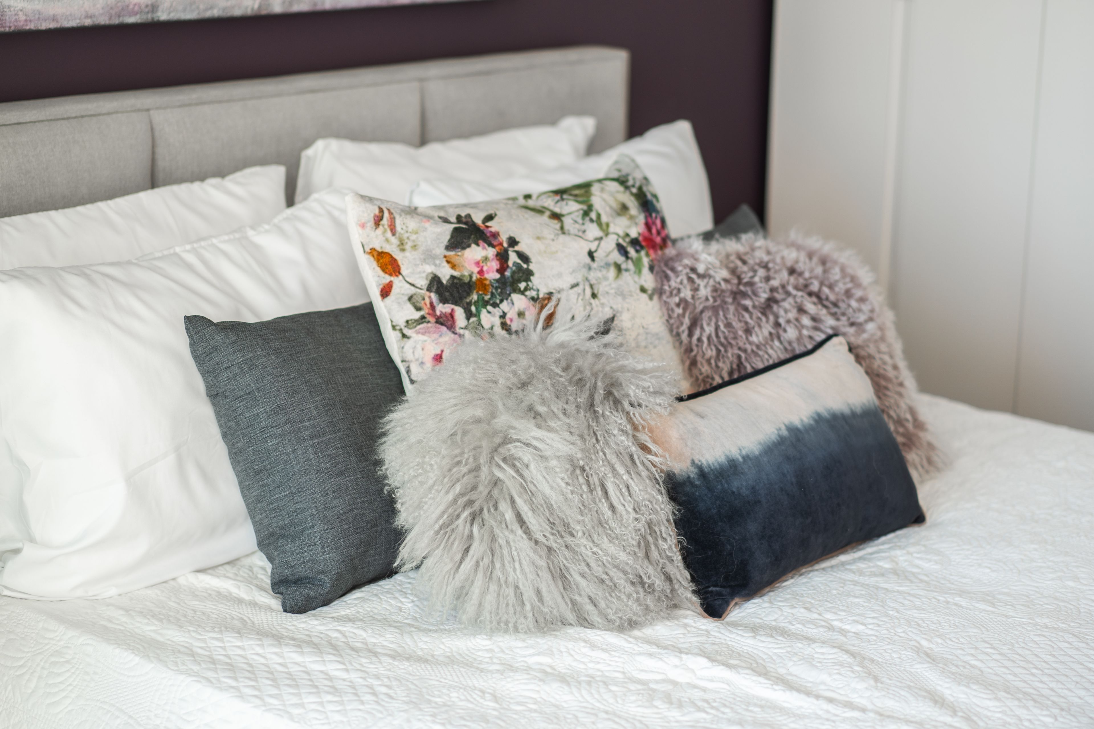 Una cama con varios almohadones, incluyendo uno floral, uno gris y uno mullido.