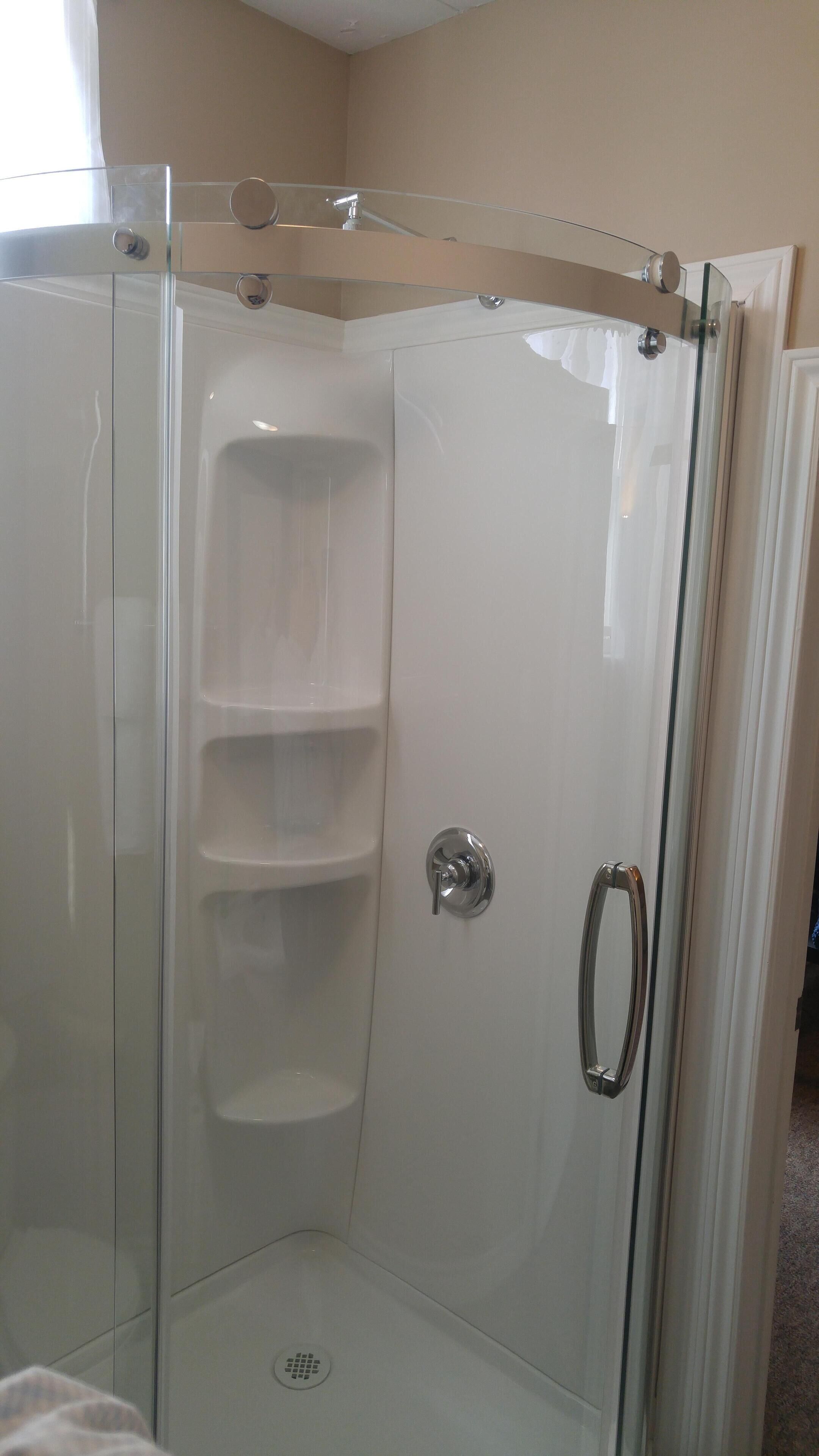 A glass-enclosed shower with a chrome handle and a white tiled wall.