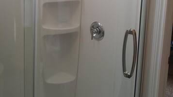 A glass-enclosed shower with a chrome handle and a white tiled wall.