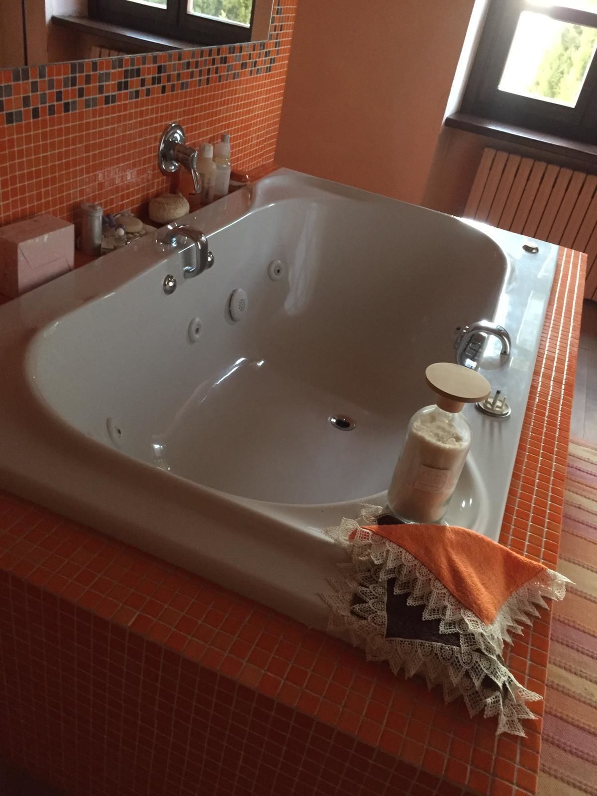 A large bathtub with a handheld showerhead, a bottle of soap, and a towel on the side.