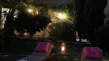 Deux chaises longues avec des coussins roses, placées dans un jardin au crépuscule.
