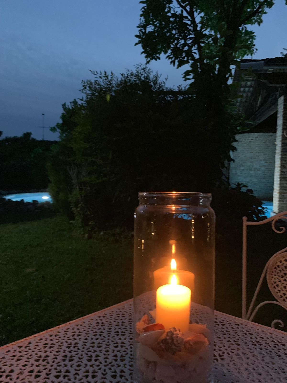 A candle in a jar placed on a table outdoors at dusk.