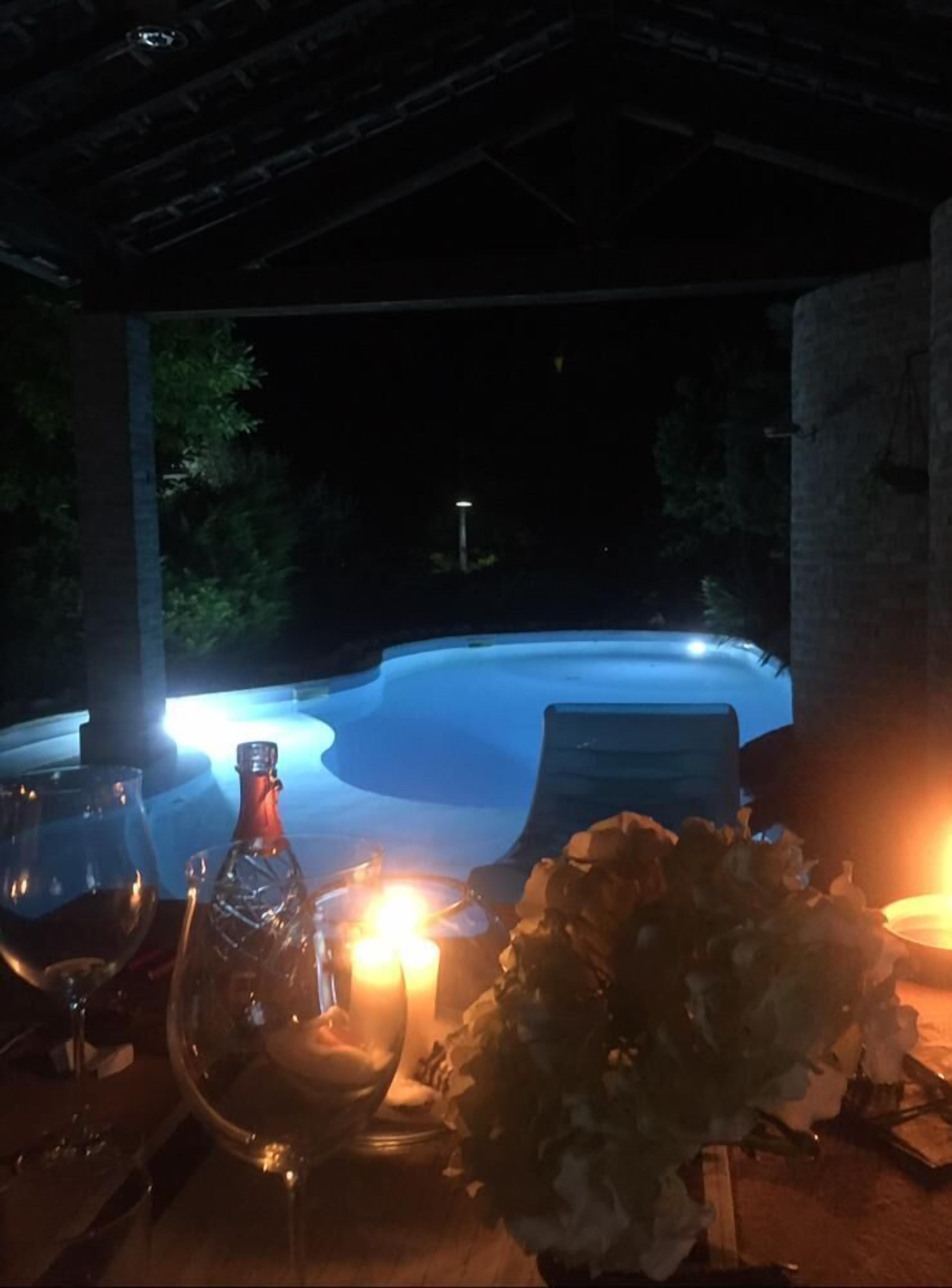 An outdoor dining area with a view of a hot tub, a candle, and a bottle of wine on a table.