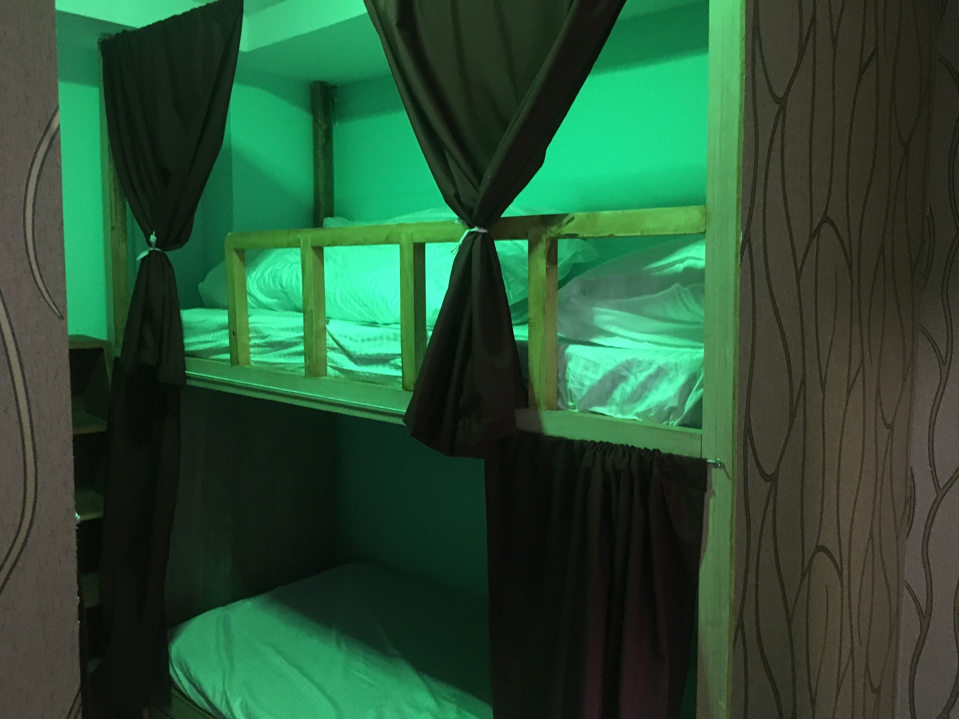 A bunk bed room with green lighting, curtains tied at the headboard, and patterned wallpaper.