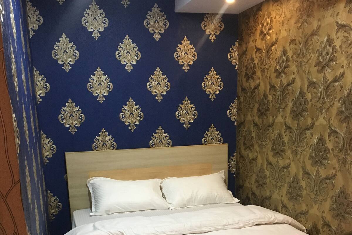 A neatly made bed with a white and pink bedspread, a wooden headboard, and a red rug at the foot of the bed.