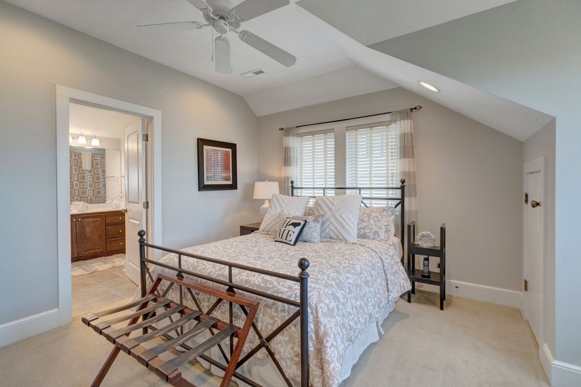 A bedroom with a bed, a nightstand, a lamp, a ceiling fan, and a window with blinds.