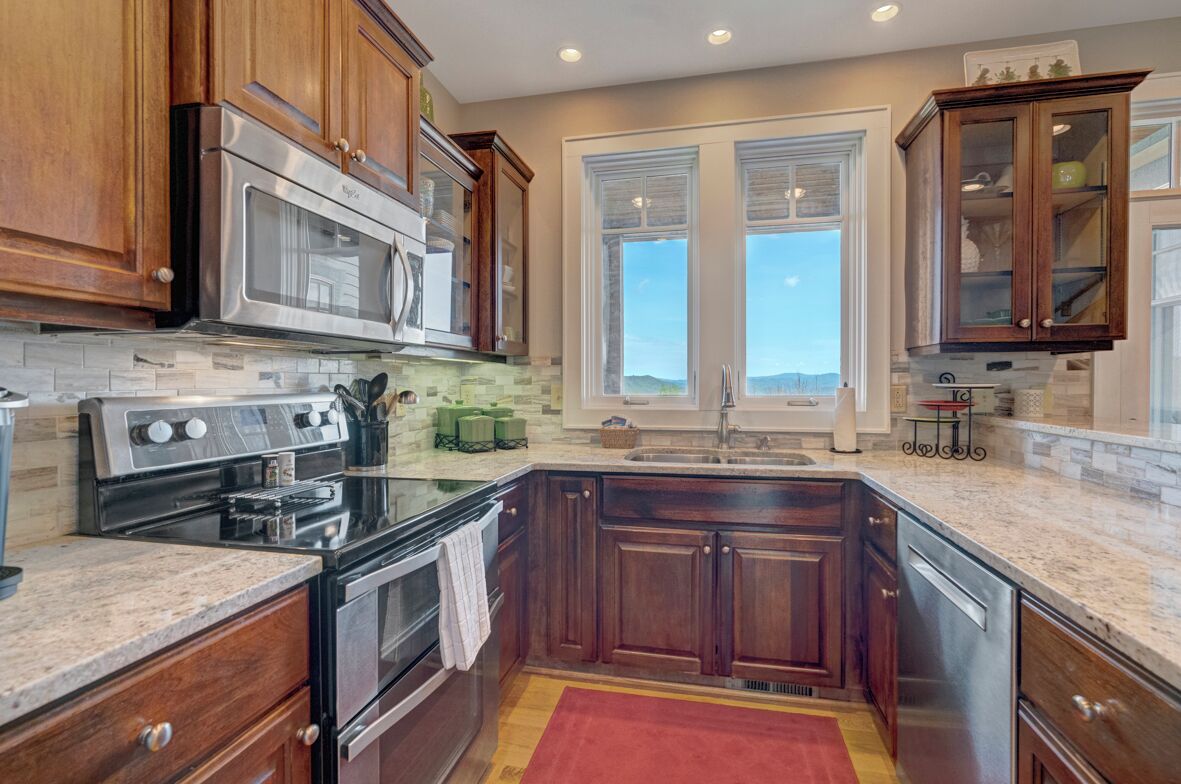 A kitchen with wooden cabinets, stainless steel appliances, a granite countertop, and a red rug.