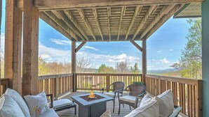 Un espacio de estar al aire libre con techo, una chimenea, una terraza de madera y vistas al paisaje.