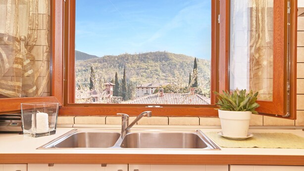 A kitchen with a double sink, a potted plant, and a view of a mountain landscape through a window. - Appartamento Il Moresine (Roe Volciano)