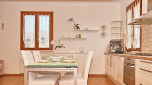 A modern kitchen with white cabinetry, a dining table with chairs, and a window with sheer curtains. - Appartamento Il Moresine (Roe Volciano)