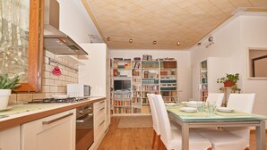 A modern kitchen with a dining area, wooden cabinets, a stove, and a bookshelf filled with books. - Appartamento Il Moresine (Roe Volciano)