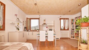 A spacious room with a bed, a dining area with chairs, a kitchen with a stove, and a bookshelf. - Appartamento Il Moresine (Roe Volciano)