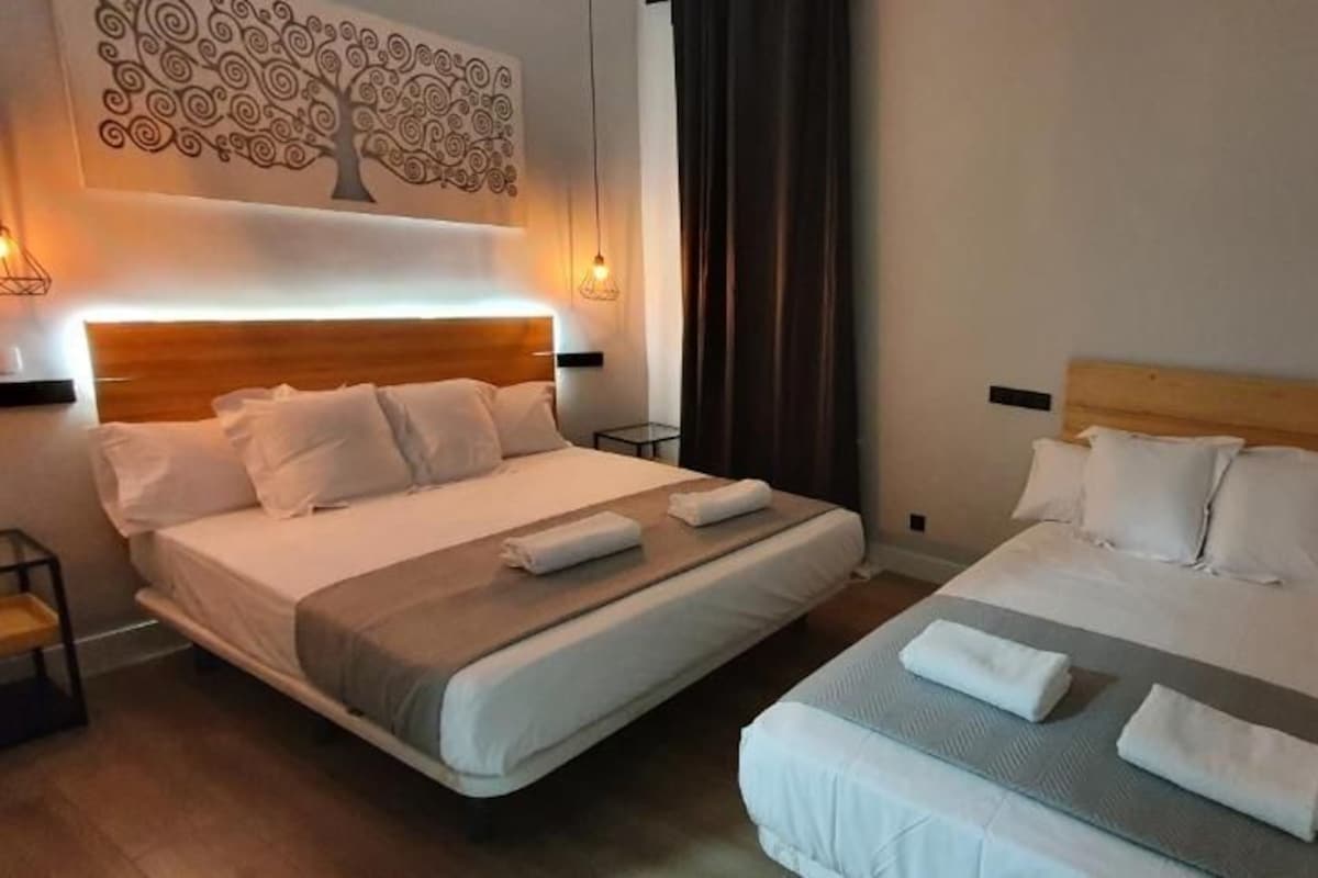 Una camera d'albergo con due letti, una TV a parete e un quadro decorativo con un albero.