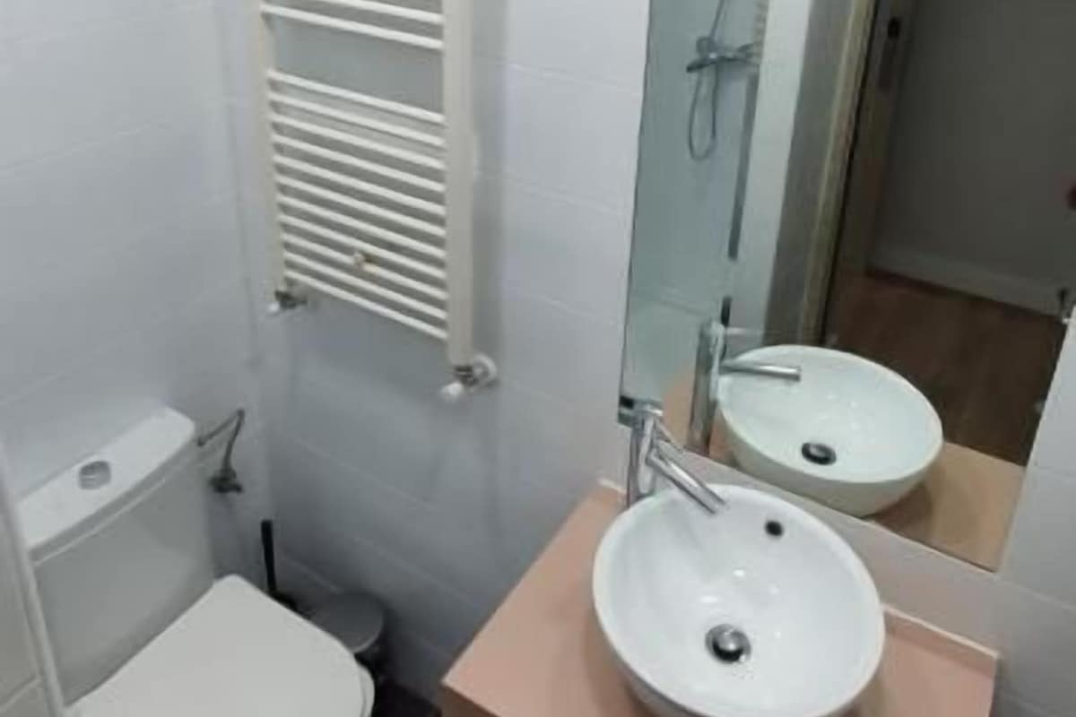Un baño pequeño con inodoro, lavamanos, espejo y toallero.