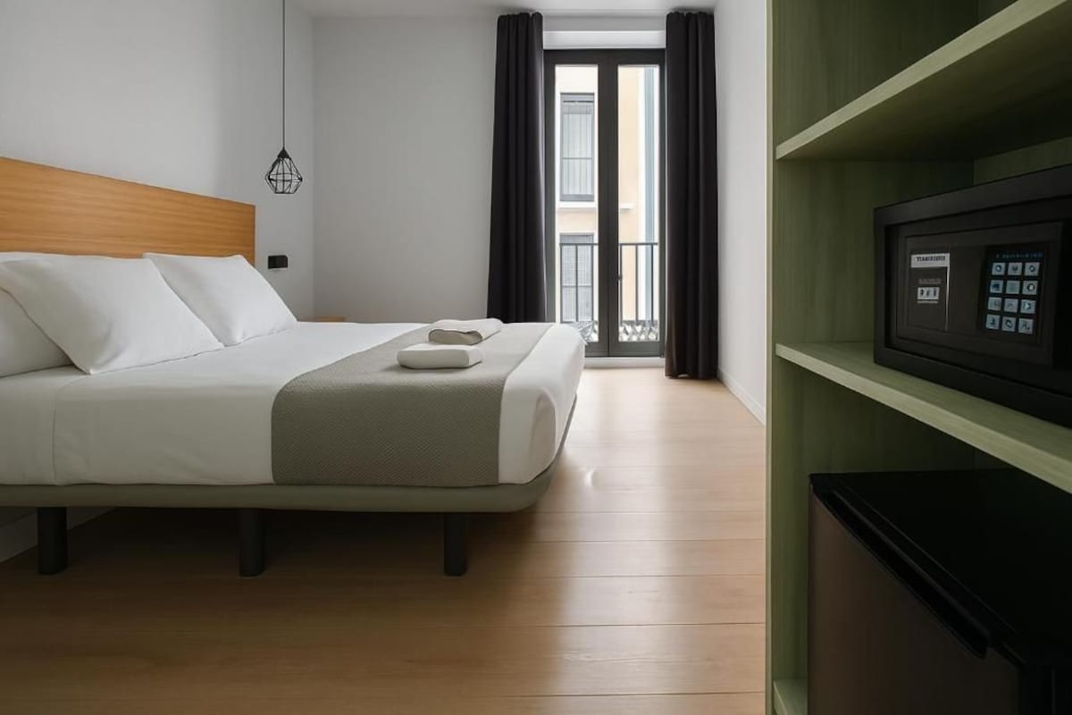A hotel room with a bed, a television, and a view of the outside.