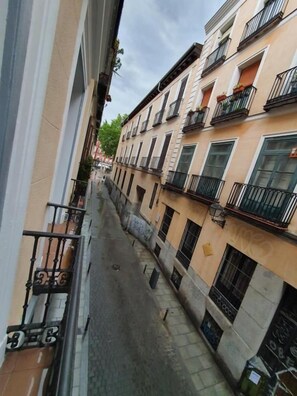 Una stretta via tra edifici con balconi, cielo sereno e un cartello stradale ben visibile.