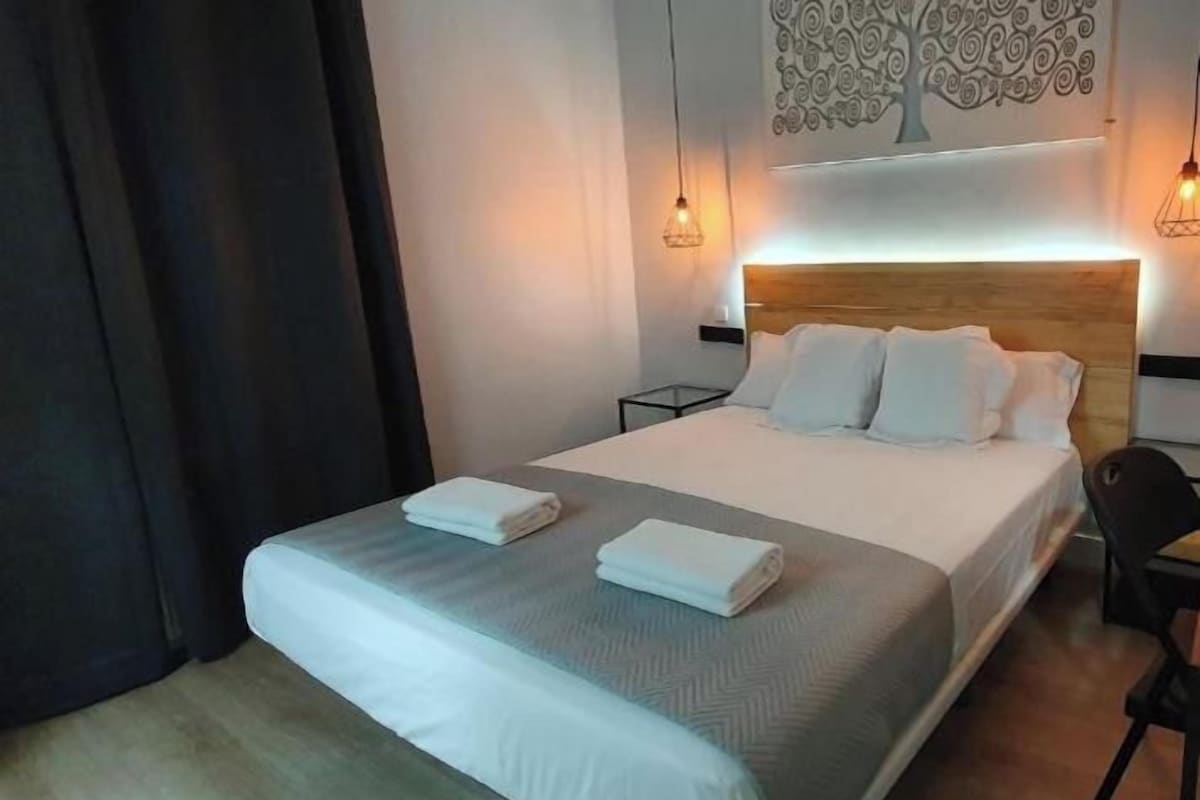 A hotel room with a large bed, a headboard, two bedside tables, a chair, and a wall-mounted artwork.