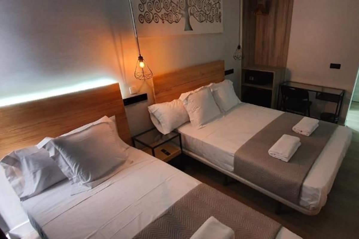 A hotel room with two beds, a nightstand, a lamp, and a wall-mounted artwork.