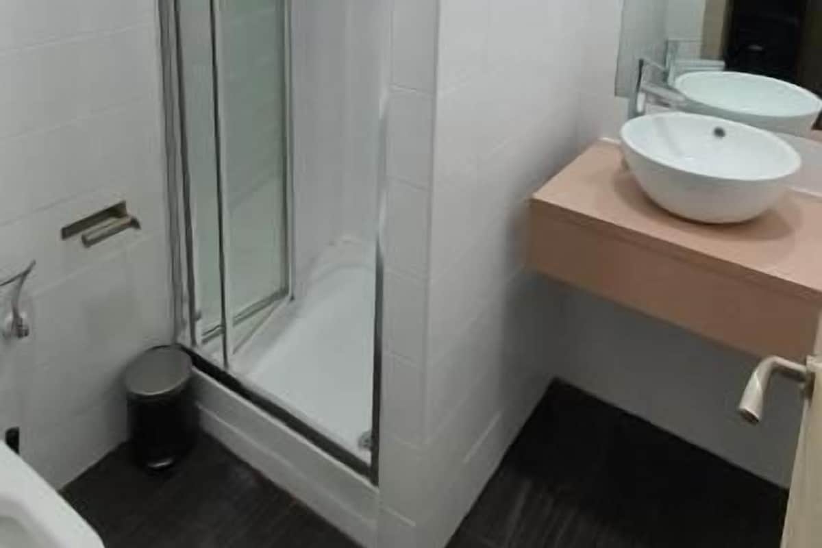 A bathroom with a glass-enclosed shower, a white sink, and a mirror on a wooden countertop.