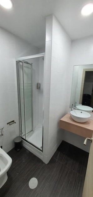 Un bagno con doccia vetrata, lavandino bianco e specchio su un piano in legno.
