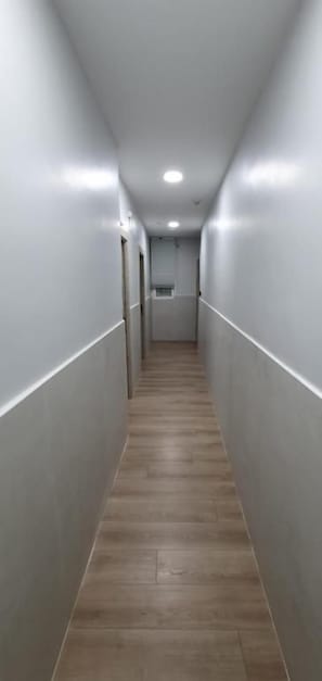 Un corridoio stretto, ben illuminato, con pavimento in legno e pareti bianche.