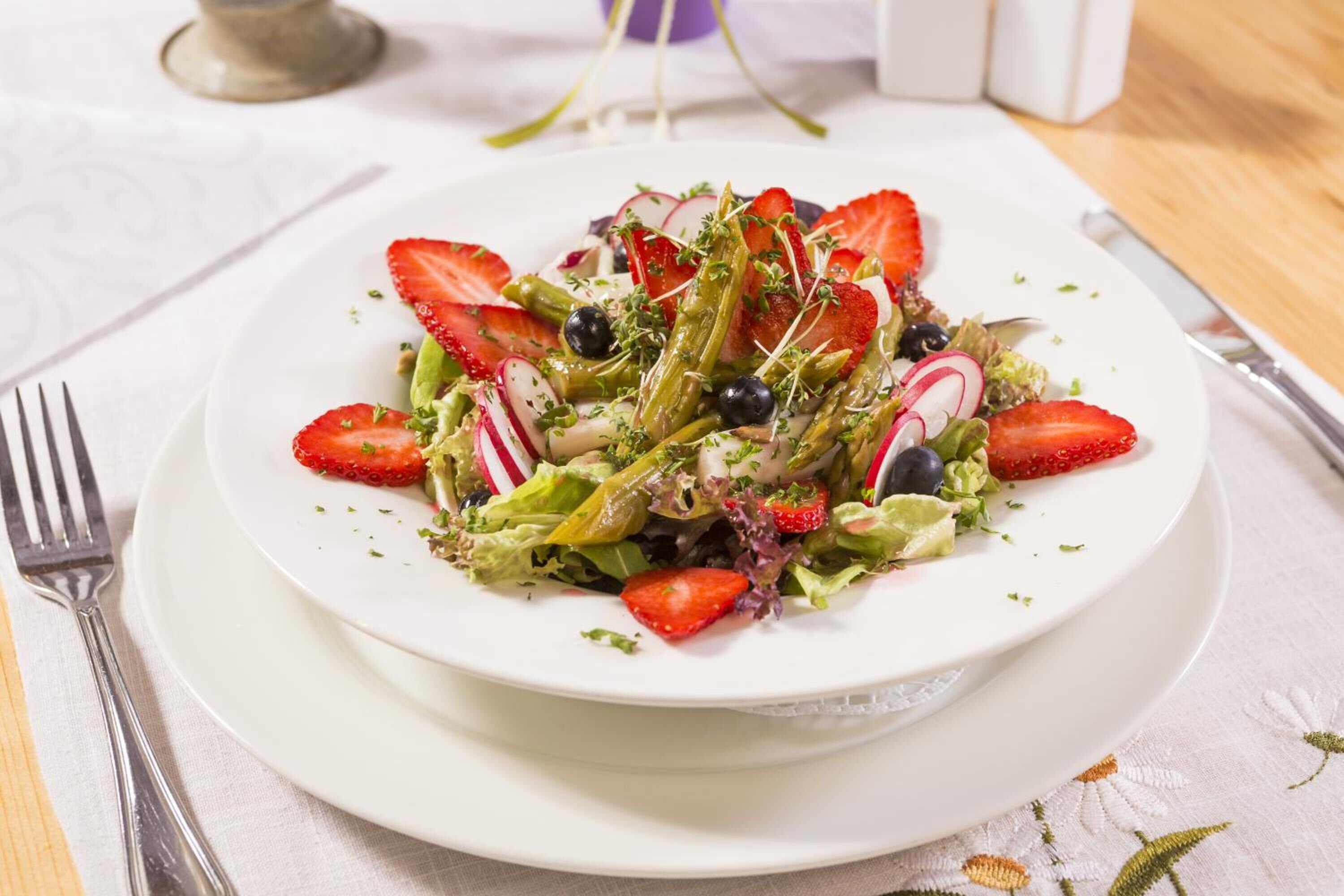 A white plate with a salad on a white tablecloth.