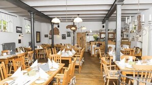 Um restaurante com mesas e cadeiras de madeira, luminárias pendentes e detalhes em tijolo nas paredes.