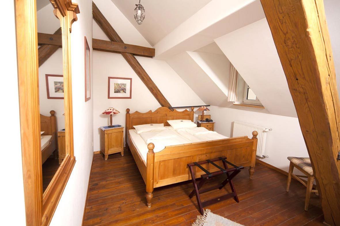 A bedroom with a wooden bed, a nightstand, a chair, and a window.