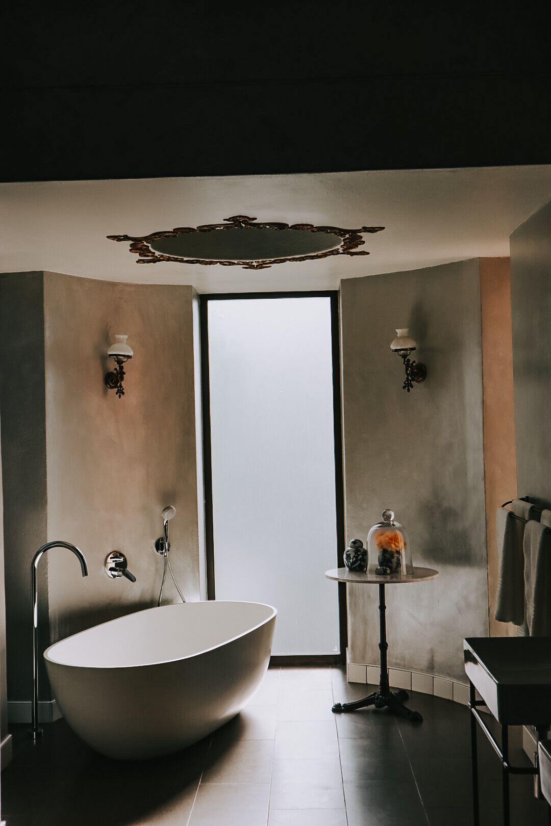 A modern bathroom with a freestanding bathtub, a small table with decorative items, and wall-mounted lights.