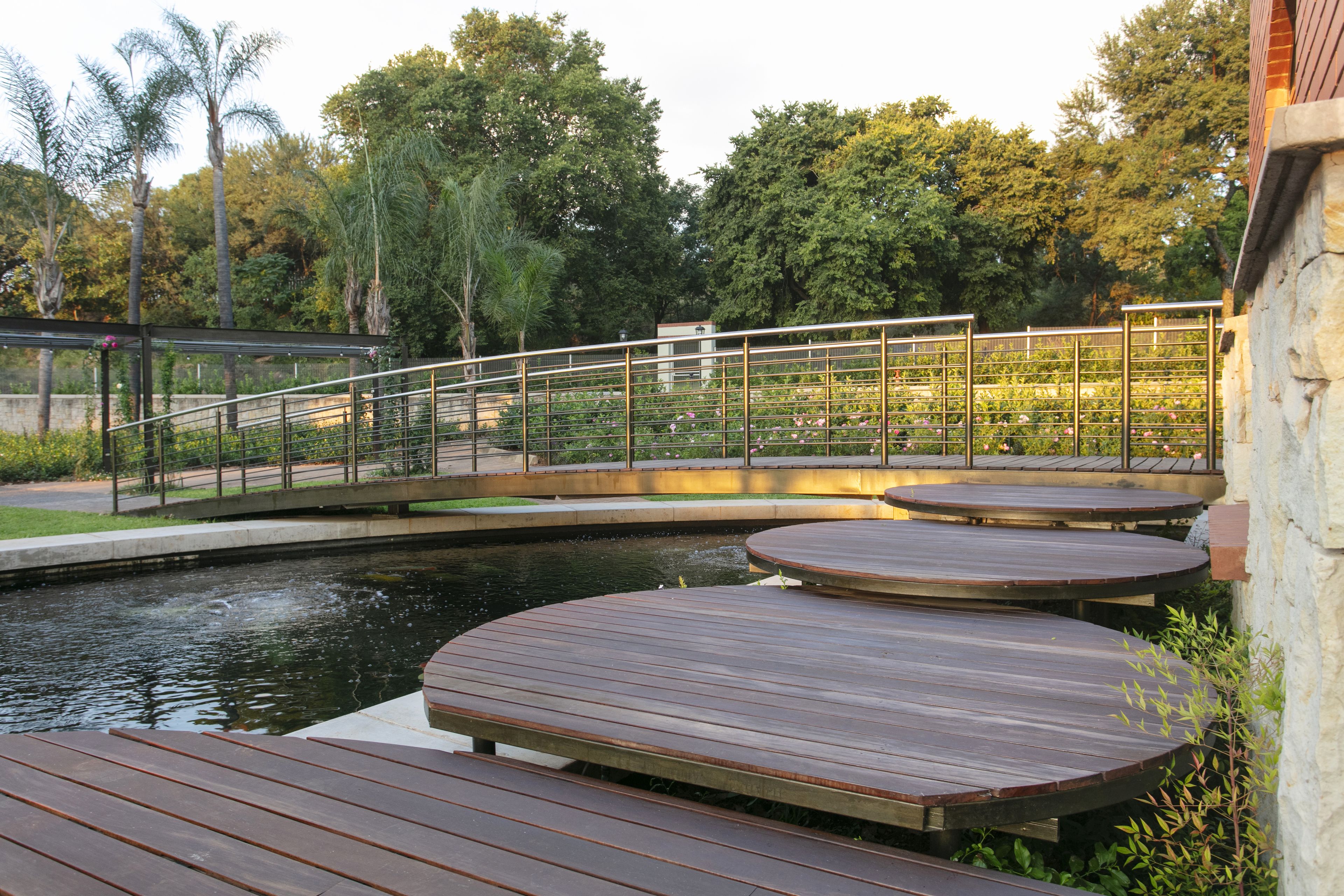 Une terrasse en bois avec une rambarde en métal, donnant sur une étendue d’eau, et entourée de verdure et d’arbres.
