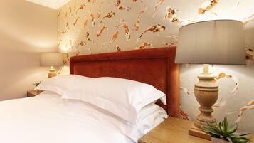 A neatly made bed with white linens, a wooden nightstand with a lamp, and a wall with a fish pattern.