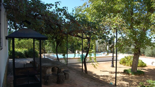 A covered outdoor seating area with a pool in the background. - El Garrotal Rural Cottage (Sevilla)