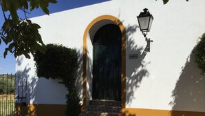 A building with a white facade, a black door with a yellow arch, and a tiled staircase leading to the entrance. - El Garrotal Rural Cottage (Sevilla)