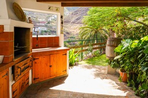 A kitchen with a brick oven, wooden cabinets, and a view of a lush garden and mountains. - Casa La Poyata- Taganana (Santa Cruz de Tenerife)
