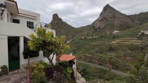 Un bâtiment blanc avec une porte verte et un toit recouvert de tuiles rouges, qui surplombe un paysage montagneux avec un sommet particulièrement imposant.