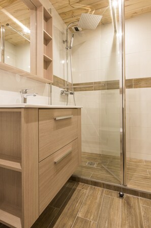 Une salle de bain moderne avec un meuble-lavabo en bois, une cabine de douche en verre et un sol carrelé.