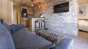 Un espace de vie moderne avec un plafond en bois, un mur en pierre et un téléviseur à écran plat fixé au-dessus du plan de travail de la cuisine.