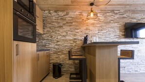Une cuisine moderne avec des armoires en bois, un four encastré, un mur de crédence en pierre et un plan de travail noir.