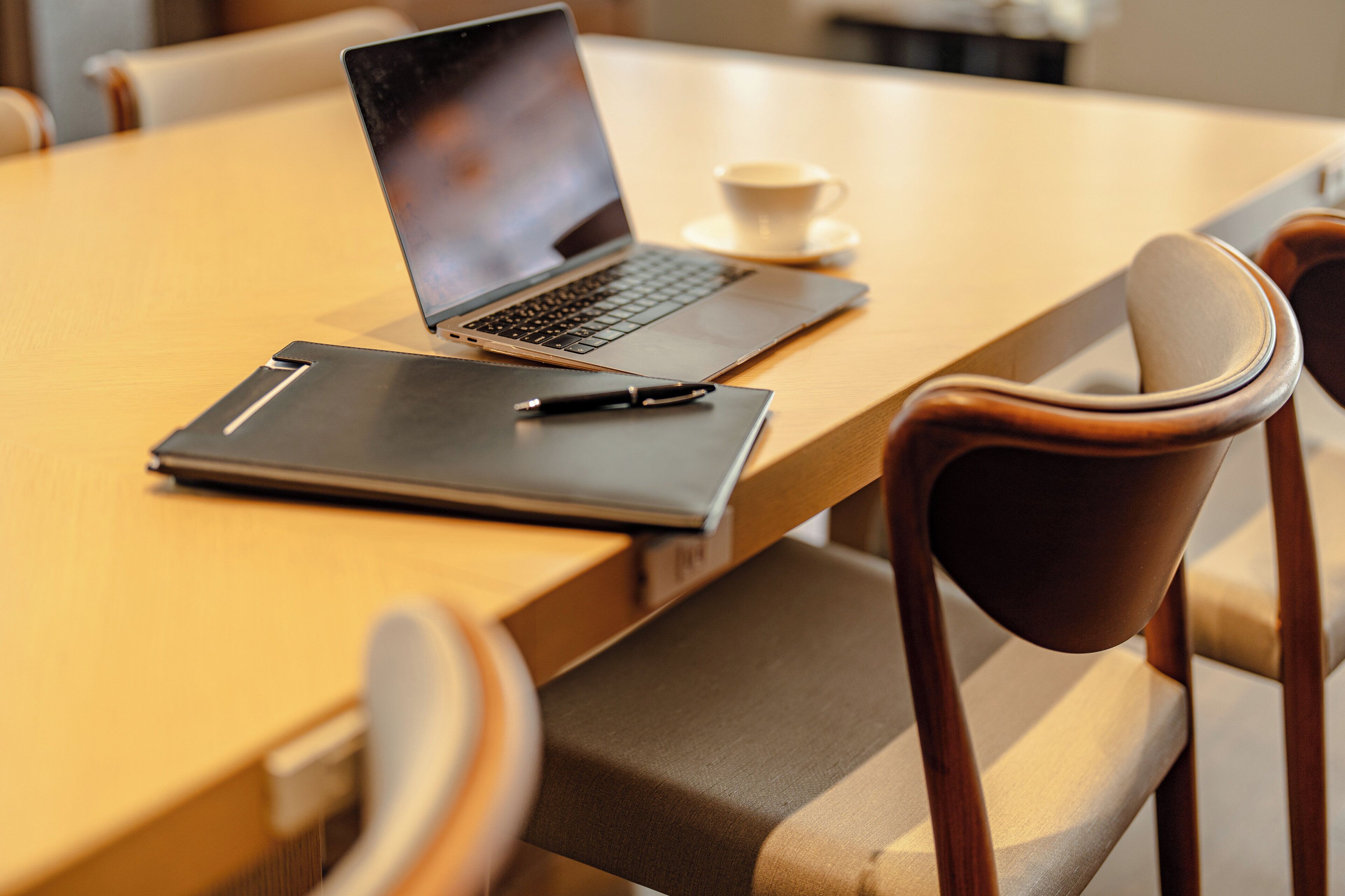 Una laptop sobre una mesa de madera, con una taza y un bolígrafo.