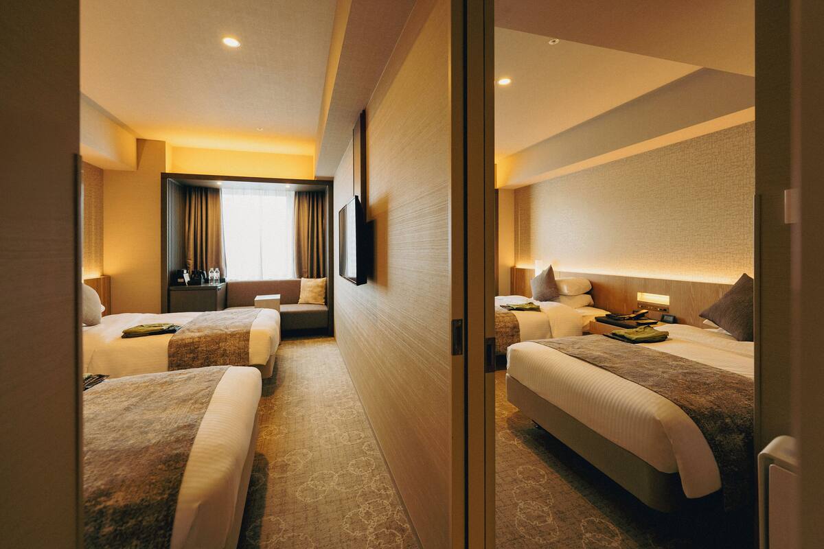 A hotel room with two beds, a desk, a chair, a TV, and a window with curtains.