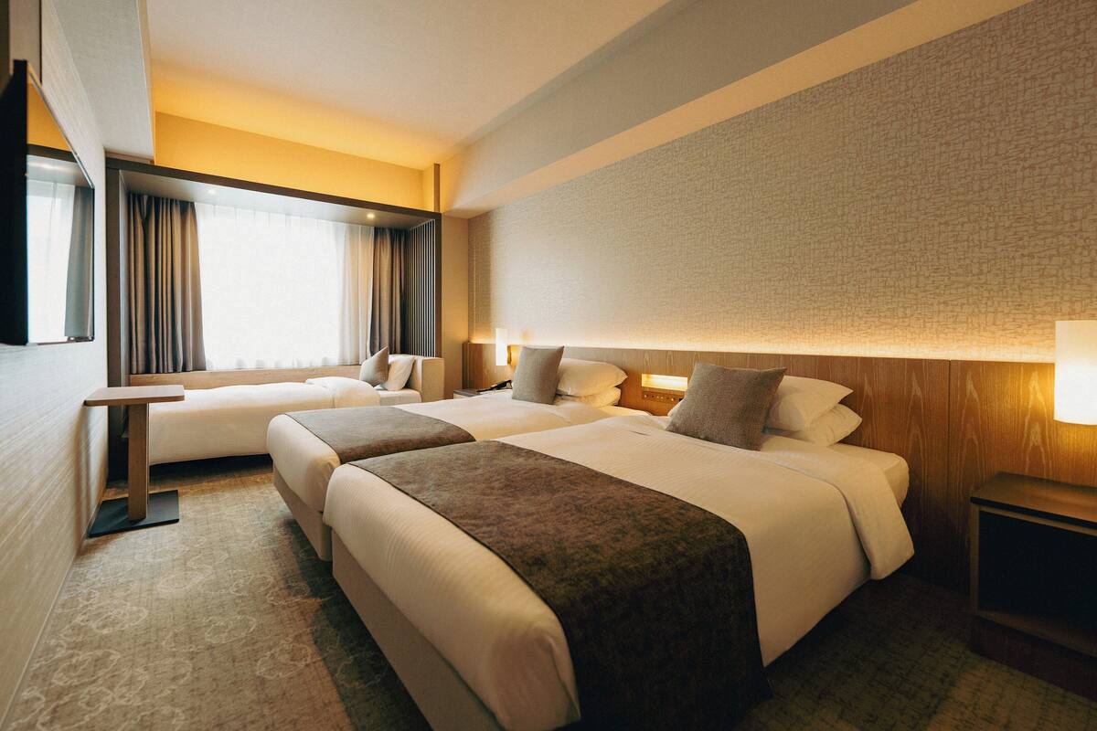 A hotel room with two beds, a desk, and a large window with curtains.