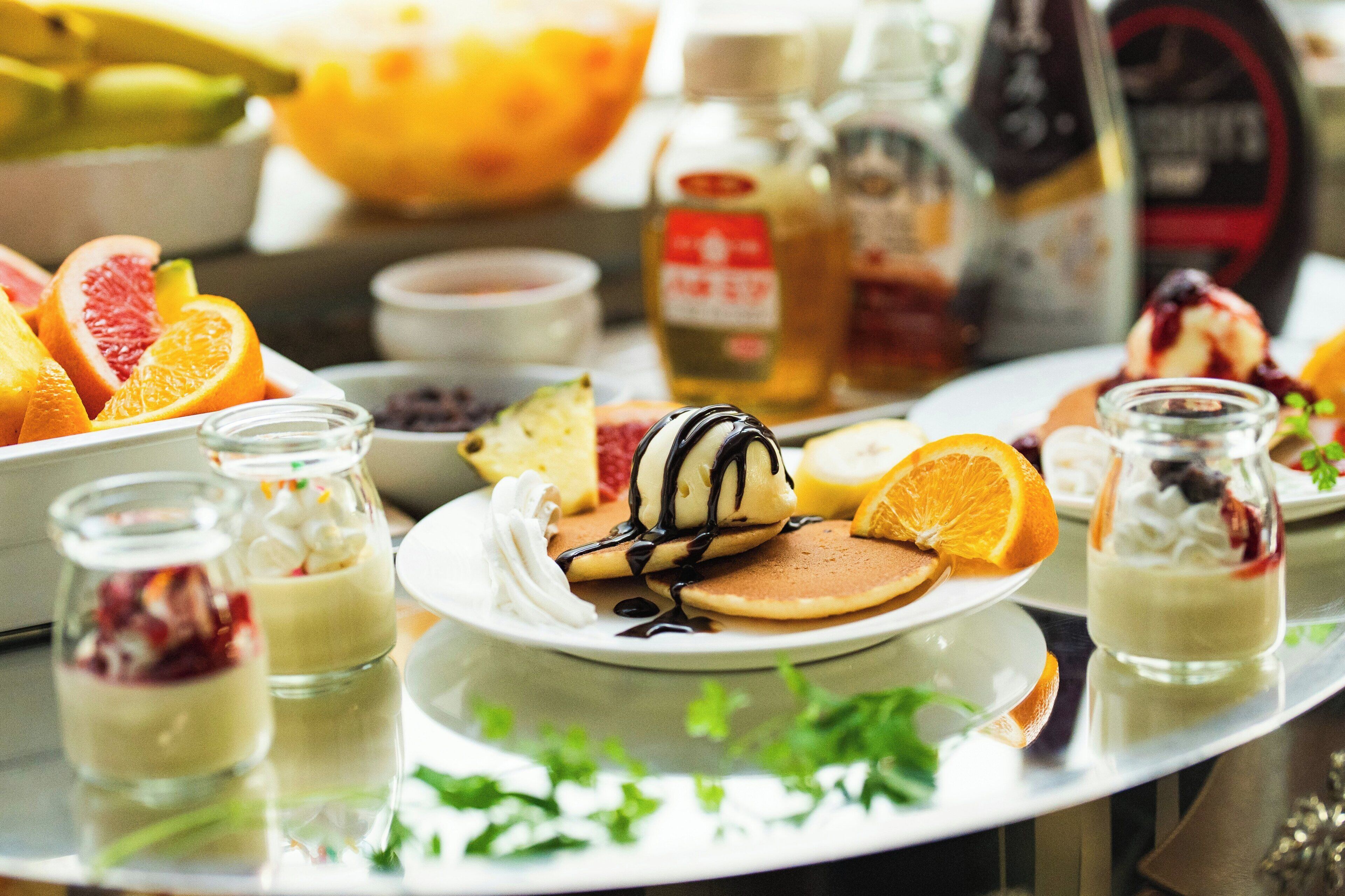 A breakfast spread with pancakes, fruit, and desserts on a table.