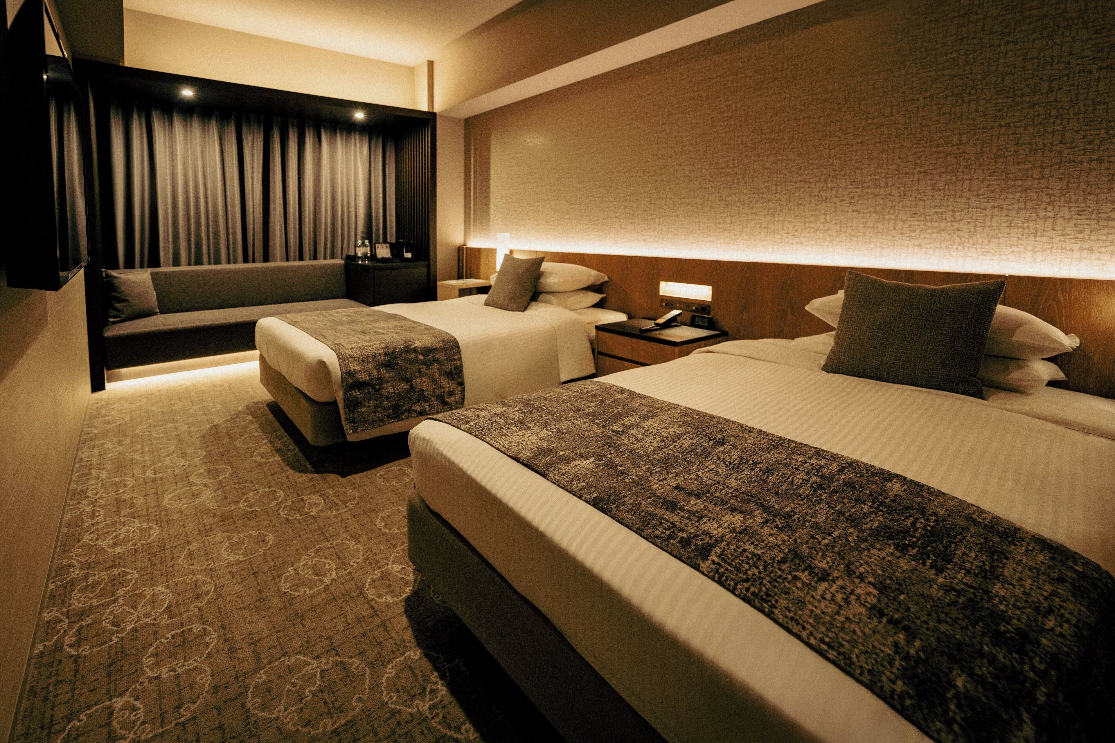 Habitación de hotel con dos camas, un sofá, un escritorio y un ventanal con cortinas.