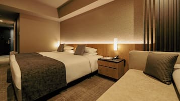 A modern hotel room with a large bed, a bedside table with a lamp, and a sofa.