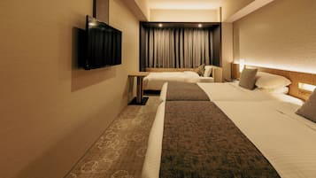 A hotel room with two beds, a flat-screen TV mounted on the wall, a bedside table, and a large window with curtains.