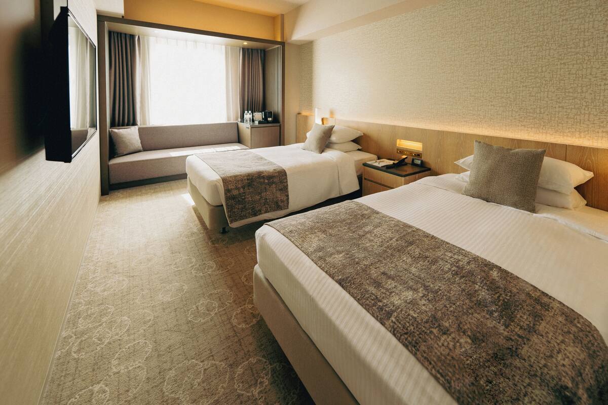A hotel room with two beds, a sofa, a TV, and a desk with a lamp.