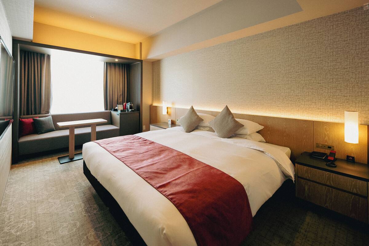 A hotel room with a large bed, a desk, and a seating area.